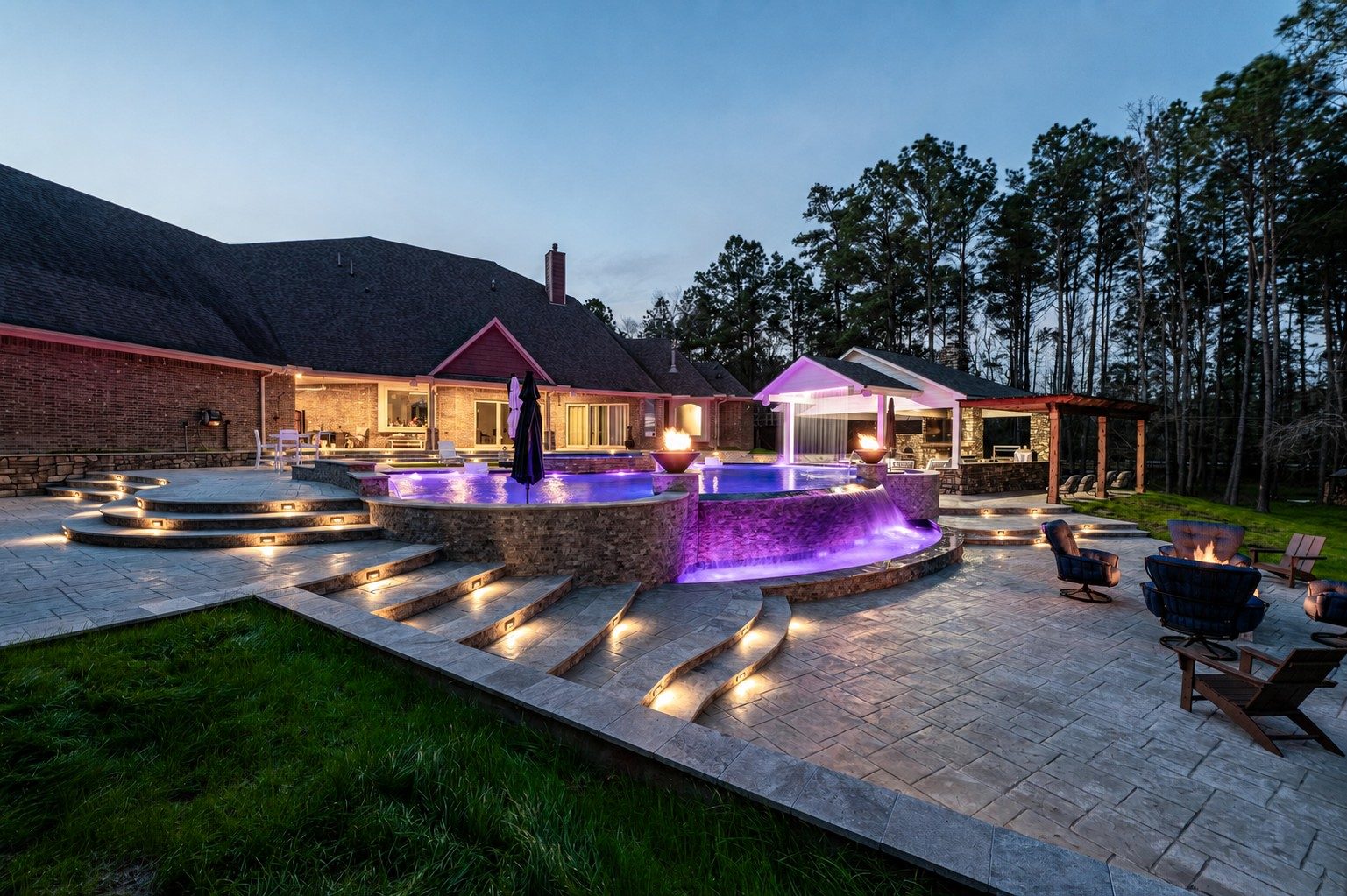 A Reef Pools and Spas freeform pool, spa, and pavilion lit at dusk against the pine treeline in Montgomery County, Texas